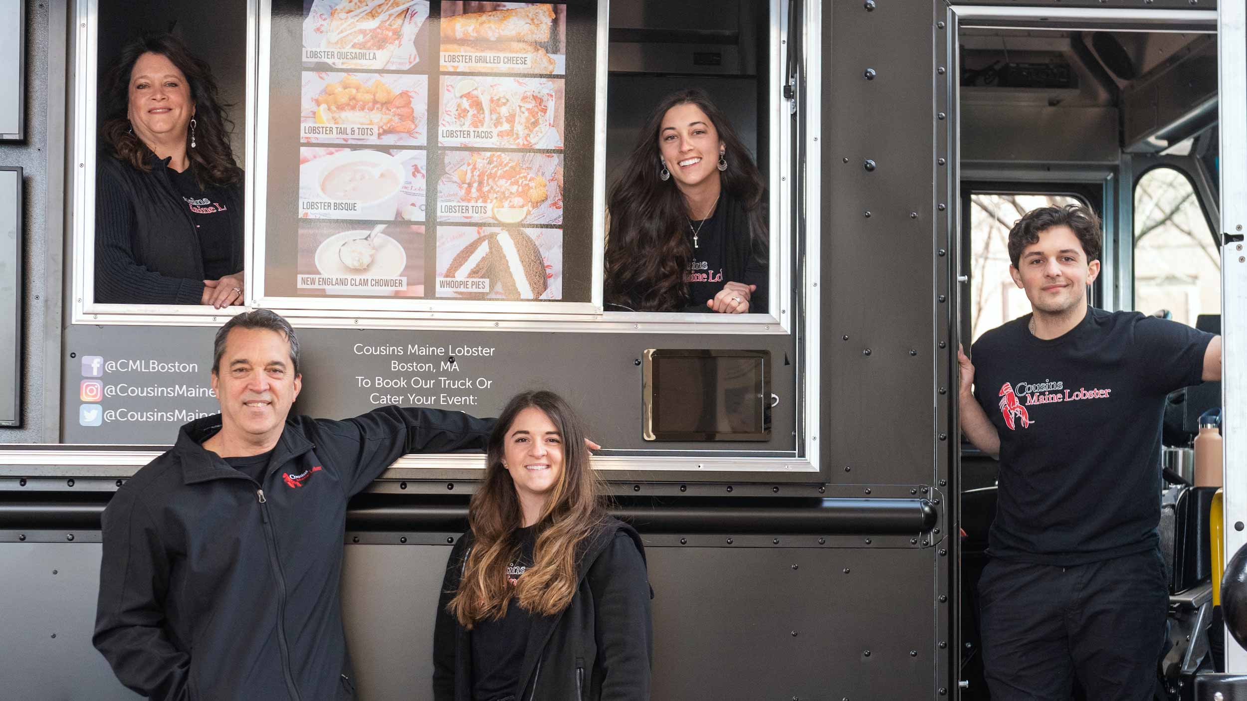 A family of Cousins Maine Lobster Boston owners standing inside and outside their food truck.