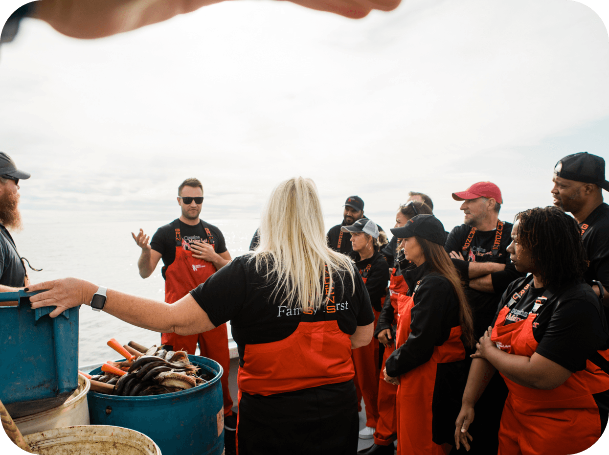 An image of Cousins Maine Lobster family members on a boat in Maine, listening to Cousin Jim speak as they are out training and fishing.